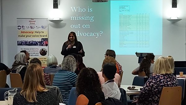 Nahida, our Advocacy Director, speaking at an event in front of people seated at round tables. She is holding a microphone.