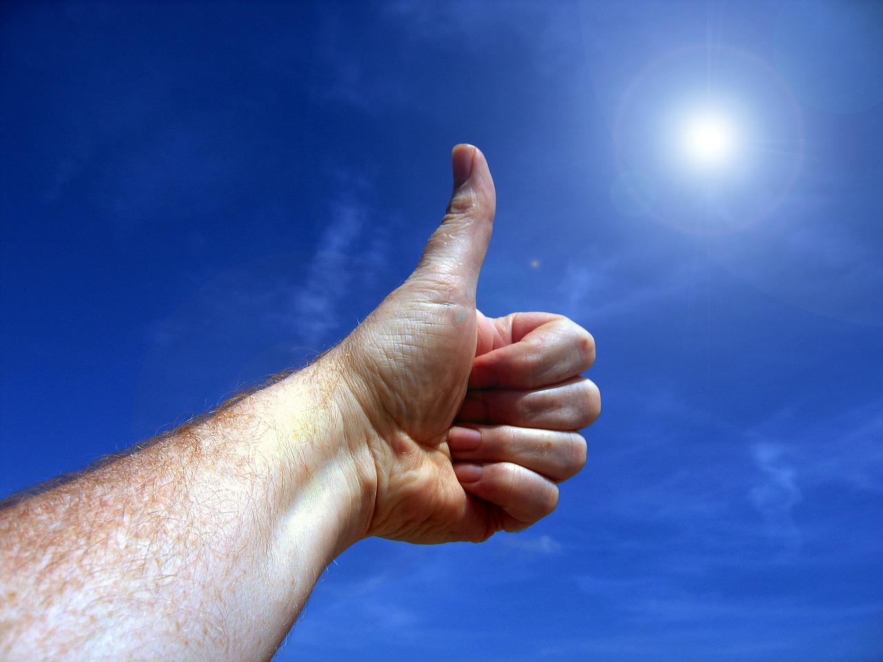 Picture of someone giving a thumbs up sign towards a blue sky with the Sun in the right-hand corner