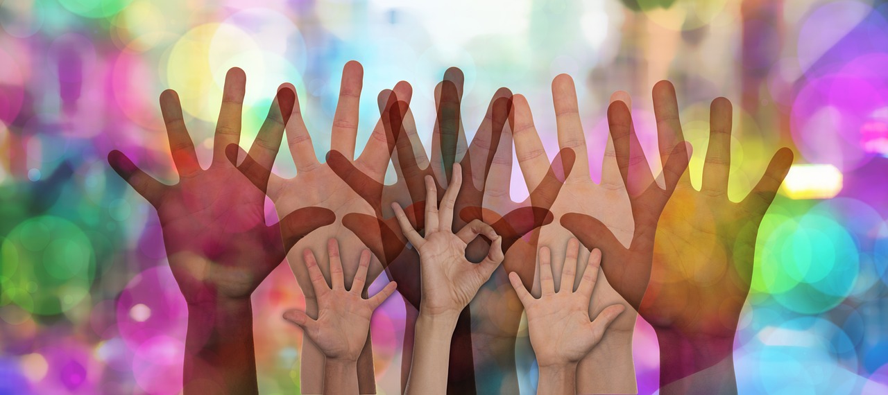 A number of different-sized hands being raised to show that they want to help. They are all in front of a background of different coloured shapes.