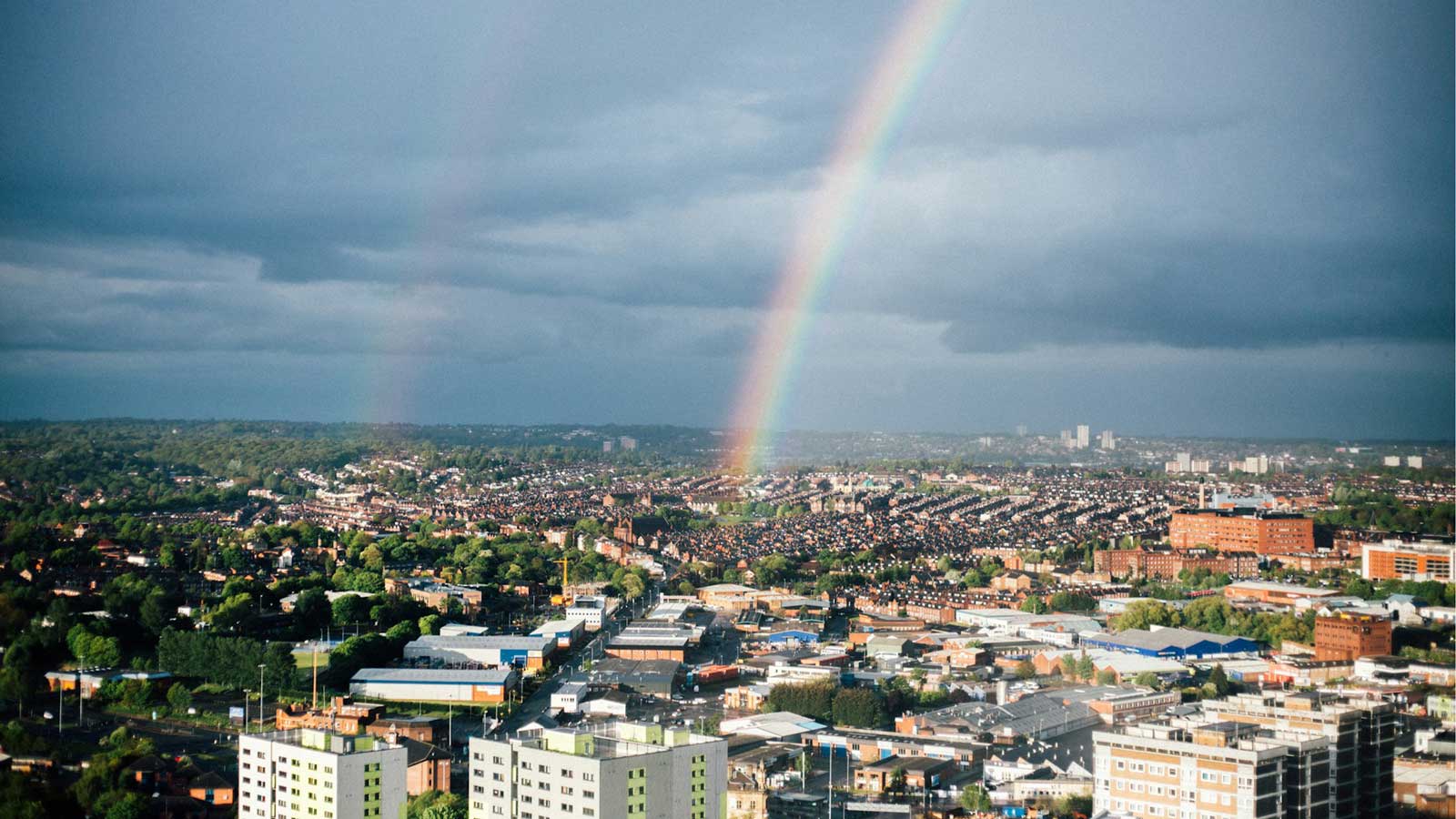 An image of the Leeds skyline, with a blue-grey sky and rainbow above.