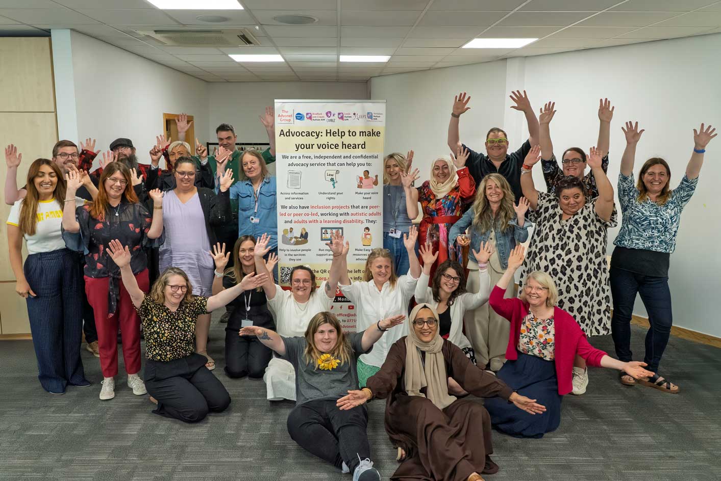 A photo of Advonet Group staff and other people with their arms raised in celebration. They are stood around a stand-up banner with The Advonet Group's logo on it.