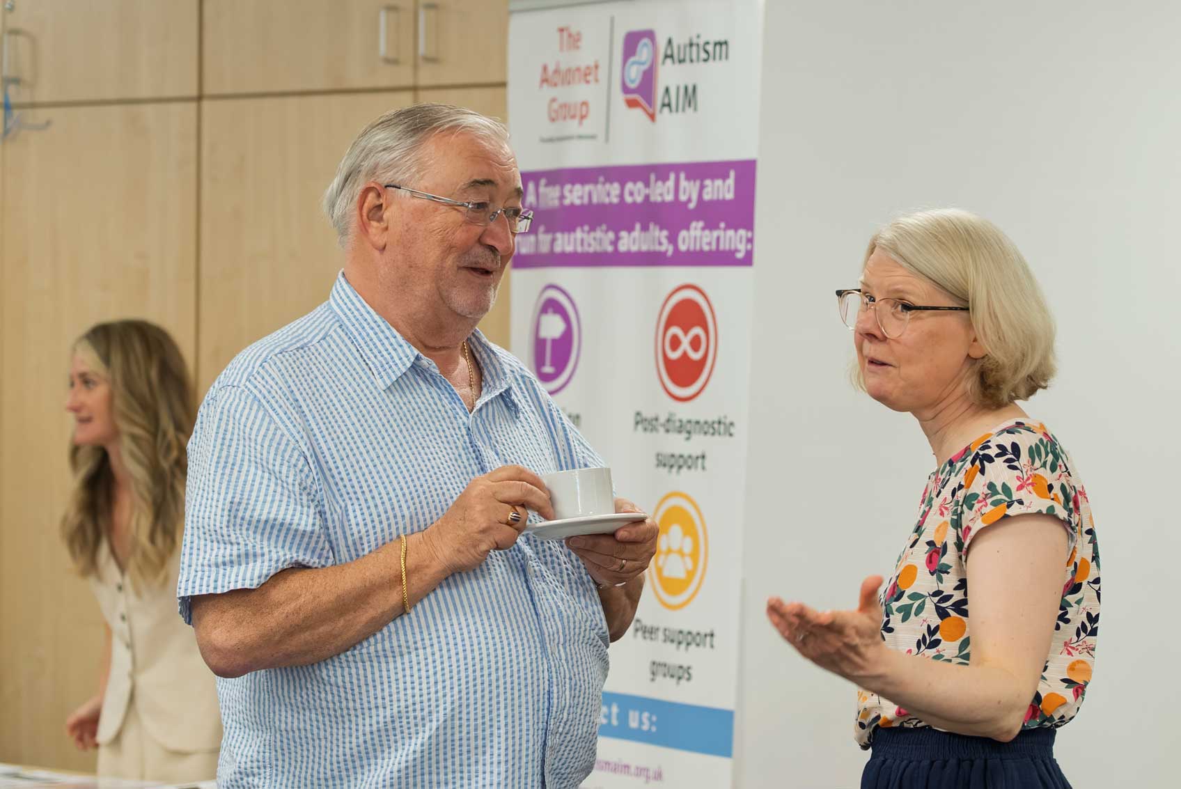 A photo of Peter, our Chair, talking to one of our staff team. Peter is holding a cup of tea.